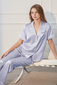 Model in lilac MANITO Authentic Short Sleeve Pajama Set seated on a chair, showcasing silky shine and relaxed fit.