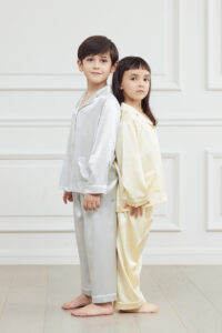 Two kids standing back-to-back in stylish Authentic Kid's Silk Pajama Sets in cream and blue.