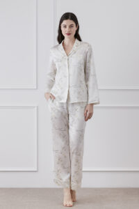 Woman displaying Princess Louise silky pajama set with delicate floral print, posing in a interior.