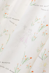Close view of silk slip dress fabric with playful 'manito' design and soft floral sketches.