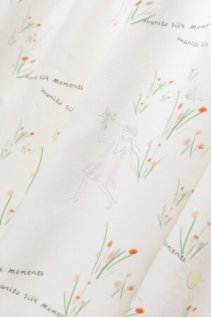 Close view of silk slip dress fabric with playful 'manito' design and soft floral sketches.