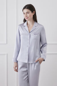 A smiling woman wearing Macaron Silk Pajama Set with purple trim and MANITO logo.
