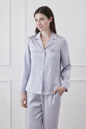 A smiling woman wearing Macaron Silk Pajama Set with purple trim and MANITO logo.