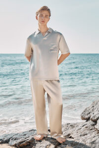 A man stands by the sea in full view, modeling the ivory-colored MANITO Remington Men's Short Sleeve Pajama Set.