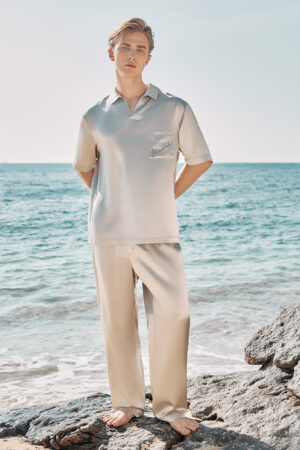 A man stands by the sea in full view, modeling the ivory-colored MANITO Remington Men's Short Sleeve Pajama Set.