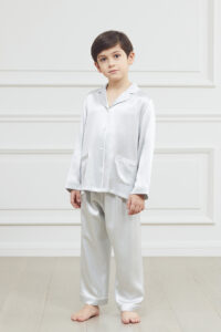 Young boy in an elegant blue silk pajama set with a sharp collar and pocket detail.