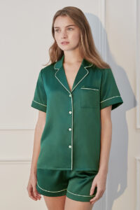 Woman lounging in Authentic Short Pajama Set, featuring dark green with white piping in a classic short-sleeve design.