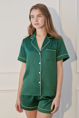 Woman lounging in Authentic Short Pajama Set, featuring dark green with white piping in a classic short-sleeve design.