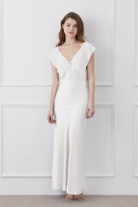Woman in a Crete Silk Midi Dress in white featuring soft ruffle details and a flattering silhouette.