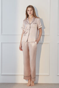 Model standing in blush pink MANITO Authentic Short Sleeve Pajama Set with black trim and soft satin texture.