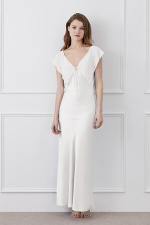Woman in a Crete Silk Midi Dress in white featuring soft ruffle details and a flattering silhouette.
