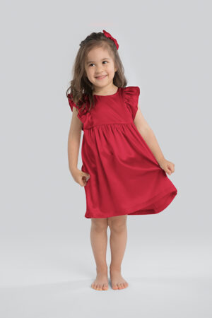 Cheerful little girl smiling in a radiant red Farbella silk nightgown with a ribbon in her hair.