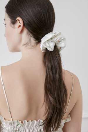 Woman wearing a Princess Louise Silk Scrunchie, featuring a floral design, styled in a simple ponytail for an elegant look.