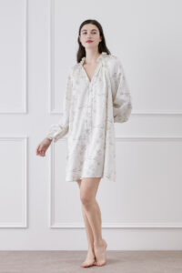 Woman in Princess Louise Silk Nightgown flaunting V-neck ruffles and lantern sleeves amid floral elegance.