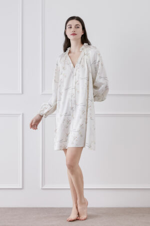 Woman in Princess Louise Silk Nightgown flaunting V-neck ruffles and lantern sleeves amid floral elegance.