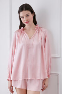 Woman in moonlight pink blouse and shorts set, smiling with ruffle trim neckline, V-neck design, and adjustable string.