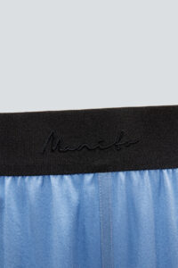 Black elastic waistband of blue Vibrant Silk Pants featuring Manito logo detail.