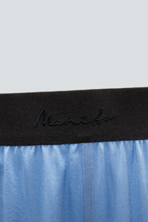 Black elastic waistband of blue Vibrant Silk Pants featuring Manito logo detail.