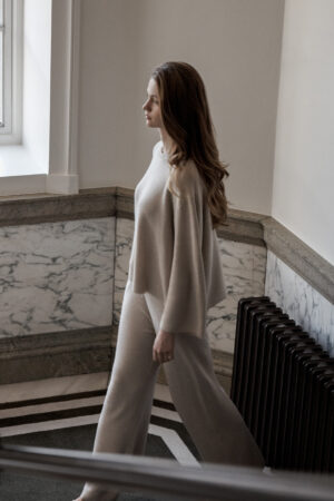 Woman ascending a marble staircase, exuding grace in a sand Silk Cashmere Set by MANITO, blending with the architectural elegance.
