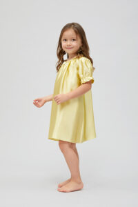 Smiling little girl in a charming soft yellow silk nightgown with puff sleeves.