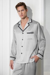 A man wearing the light grey MANITO Noir Ruban Men's Silk Pajama Set with contrasting black trim.
