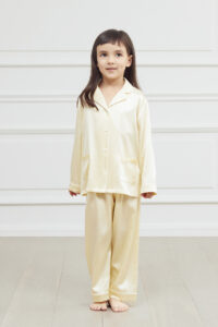 Young girl posing in a cream silk pajama set with a classic collar and button-down front.