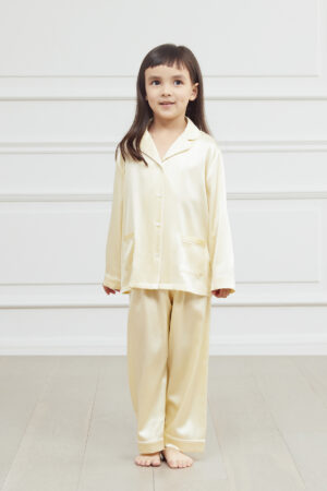 Young girl posing in a cream silk pajama set with a classic collar and button-down front.