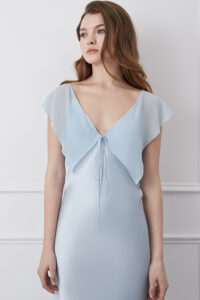 Woman in a Crete Blue Silk Midi Dress with flutter sleeves and tie front, radiating serene elegance.