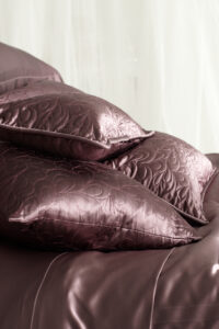 A stack of luxurious plum quilted silk pillows on a matching silk duvet, enhancing the bedroom's opulence.