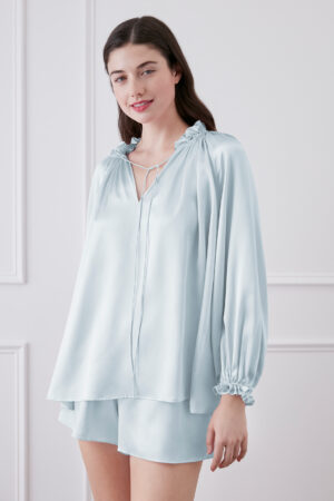Woman in blouse and shorts set slightly turned to showcase pleated design, V-neck pleats with adjustable string, and lantern sleeves cuff.