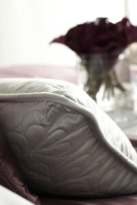 Close-up of a quilted silk pillow with a blurred burgundy rose in the background, symbolizing luxury and romance in home decor.