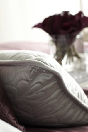 Close-up of a quilted silk pillow with a blurred burgundy rose in the background, symbolizing luxury and romance in home decor.