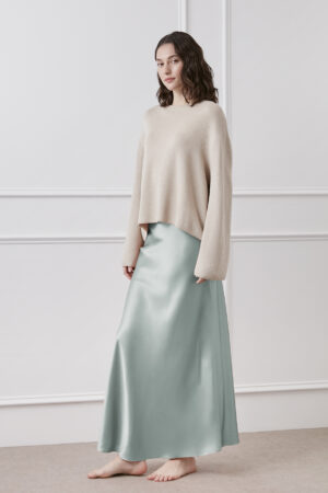 Woman presents a Muses Silk Midi Skirt in mint green with a soft neutral sweater, creating a look of understated elegance.