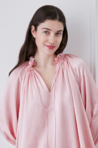 Close-up of woman in moonlight pink blouse and shorts set, showcasing V-neck ruffle trim neckline and string detail.