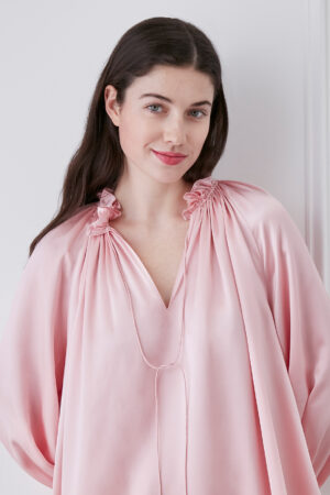 Close-up of woman in moonlight pink blouse and shorts set, showcasing V-neck ruffle trim neckline and string detail.