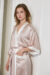 Woman wearing the Whisper short silk kimono robe in soft pink with white trim, featuring a belted waist and minimalist design.
