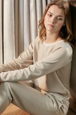 Woman seated gracefully in MANITO's sandstone silk-cashmere crew-neck loungewear set, reflecting a relaxed yet elegant aesthetic.