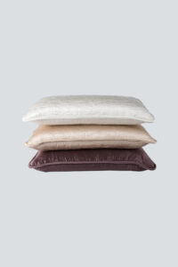 A stack of quilted lumbar silk pillows in varying shades, showcasing the MANITO brand embroidery.