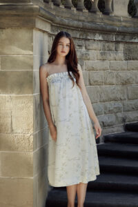 Woman in a flowing silk slip dress with a floral pattern standing by stone stairs and a balustrade.