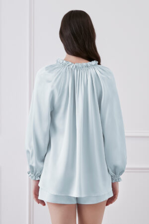 Back view of woman in baby blue blouse and shorts set, showcasing ruffle trim neckline and lantern sleeves cuffs.