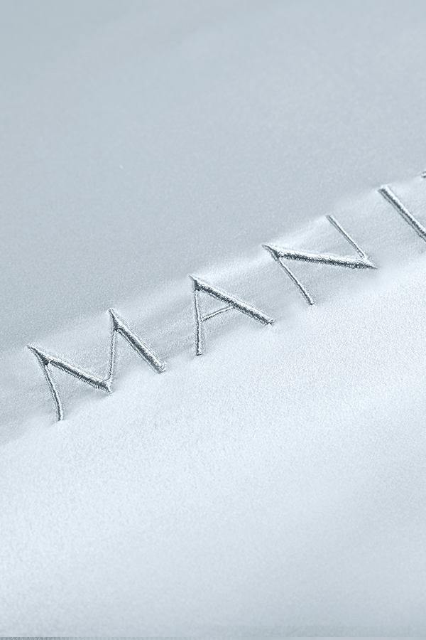 Close-up of MANITO embroidery on luxurious silk fabric, showcasing meticulous craftsmanship and elegance.