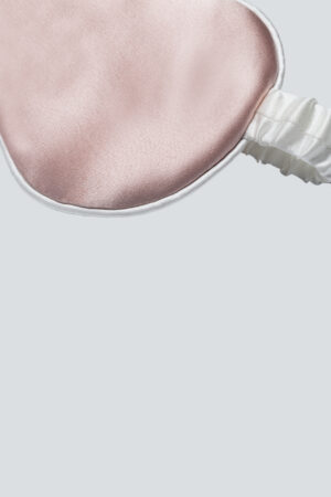 Close-up of a soft pink silk sleep mask with a ruched elastic strap for kids.