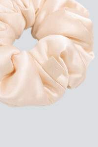 Close detail of champagne Donuts Large Silk Scrunchie showing glossy silk and branded tag texture.