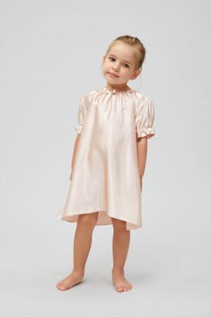 Adorable little girl posing in a chic pink silk nightgown with a sweet expression.