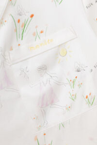 Close-up of silky pajama set pocket with 'mamito' brand name and funny sun and flower illustrations.