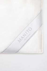 Detail of MANITO white silk filled duvet edge with logo, displaying the high-quality silk and elegant design for luxury bedding.