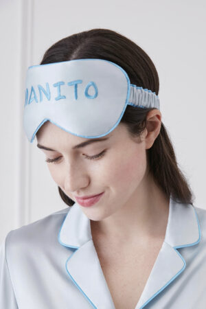 Woman wearing a light blue Macaron Silk Eye Mask with Manito branding, matching her silk pajama.