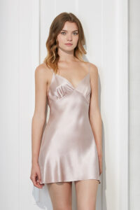 Woman presents a delicate Essential Silk Slip Dress in soft pink, embodying a soft and feminine style.