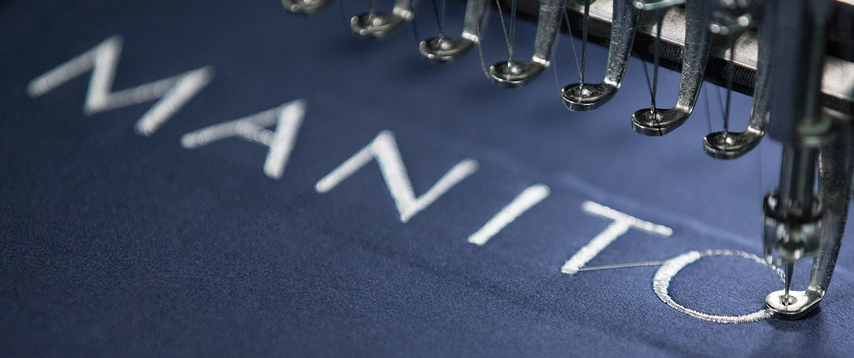 Precision embroidery machinery stitching the MANITO logo on luxurious silk fabric