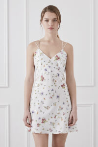 Woman wearing Lrisette Bow Midi Slip Dress in white with floral pattern and oversized front bow.